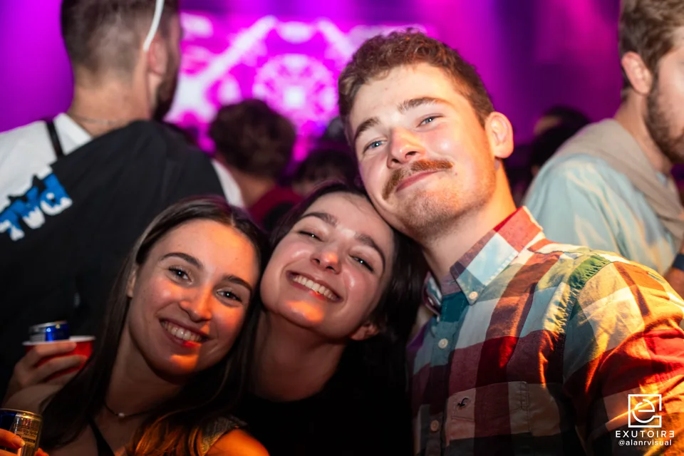 Trois personnes souriantes lors d’une soirée éclairée en violet et orange.