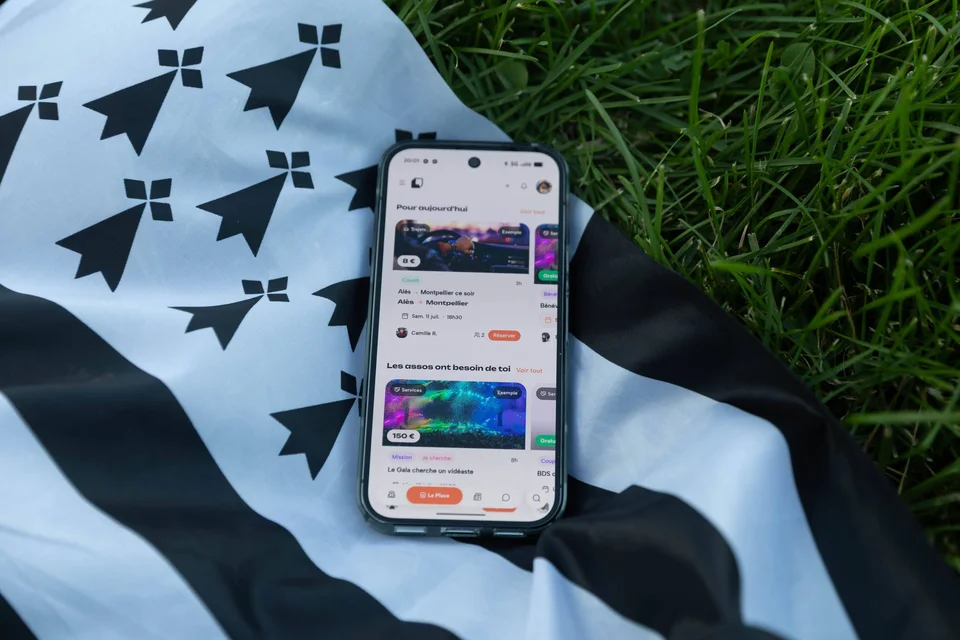 Un téléphone affichant Komi, posé sur un drapeau breton dans l’herbe.